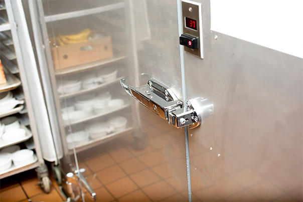 Stainless steel walk-in cooler door with a digital temperature readout, open onto shelving